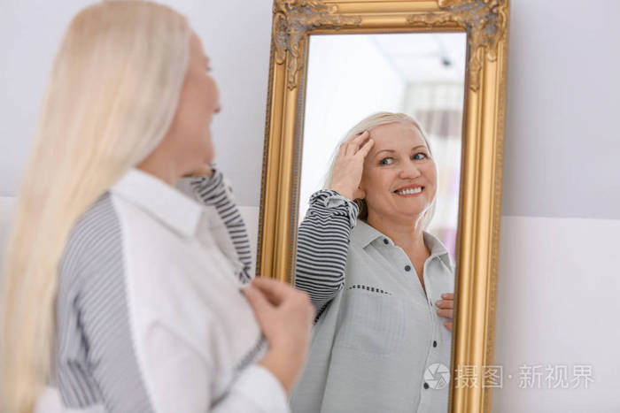 微笑成熟妇女站立在镜子附近在家