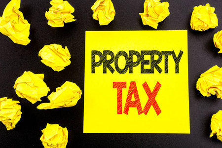 概念性手写文本, 显示物业税。房地产收入税的商业概念写在粘滞纸上。背景上折叠的黄色文件