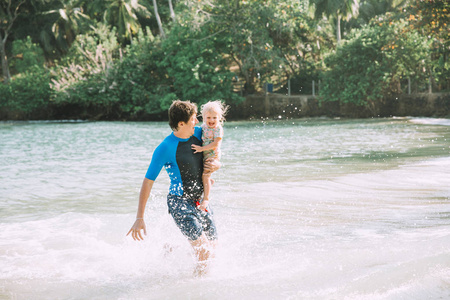 快乐的父亲抱着可爱的小女儿在热带海滩
