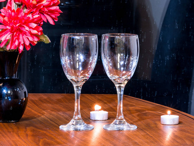 浪漫的背景照片，两个空酒杯显示在一个深色的木纹桌子上，背景是茶烛和红花。