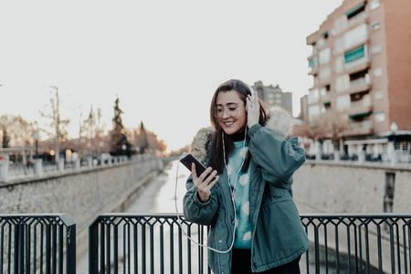 带着眼镜在街上听音乐的漂亮女人。 美丽的女人在公园里欣赏音乐。 听耳机音乐的年轻人