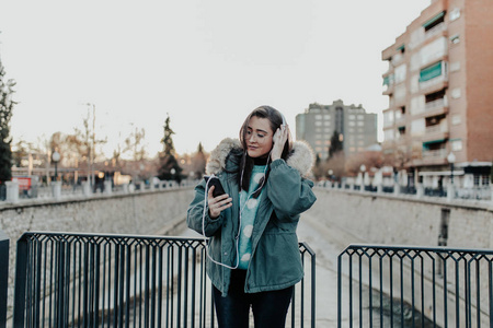 带着眼镜在街上听音乐的漂亮女人。 美丽的女人在公园里欣赏音乐。 听耳机音乐的年轻人