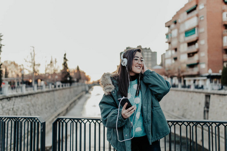 带着眼镜在街上听音乐的漂亮女人。 美丽的女人在公园里欣赏音乐。 听耳机音乐的年轻人