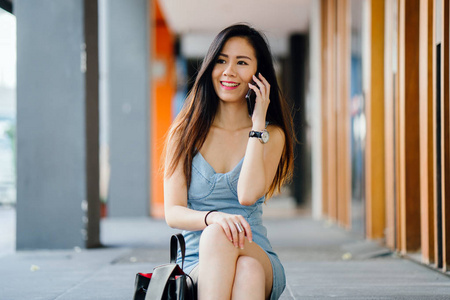 一位年轻的上镜和迷人的中国亚洲女人的肖像，她带着智能手机，而她在亚洲的一条街上等待她的约会。 她微笑着，看上去很高兴。
