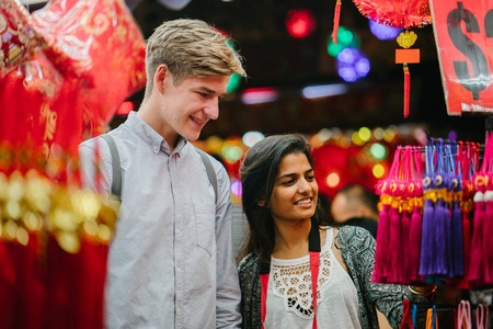 年轻的不同种族的夫妇印度妇女高加索男子在亚洲的中国新年节日期间在夜市上浏览小饰品。 他们是游客，笑着玩。