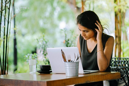 一位有吸引力和年轻的印度亚洲职业女性的坦率肖像，她在一家时髦的咖啡馆或与泰尔木家具合作的空间里用笔记本电脑工作。 她微笑着向别处