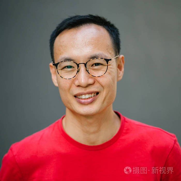 一个年轻的亚洲男人(中国日本人)靠在灰色的墙上微笑的肖像.