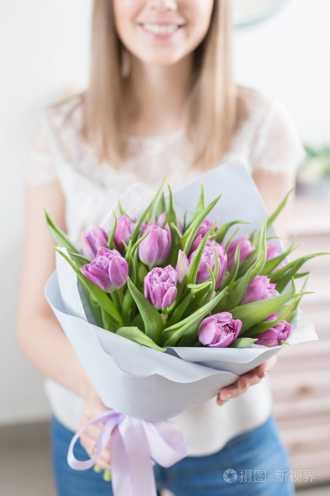 年轻快乐的女人拿着一束美丽的紫罗兰郁金香在她的手中礼物给一个微笑