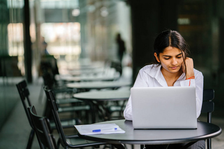 年轻的印度亚洲妇女在白天在笔记本电脑上打字和工作申请工作等。 她穿着一件专业的脆白衬衫，当她在笔记本电脑上打字时，她正在微笑