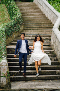 一对不同种族的恋人白天在公园的石阶上奔跑。 一个印度男人正在嫁给一个中国女人，他们高兴地跑下楼梯。