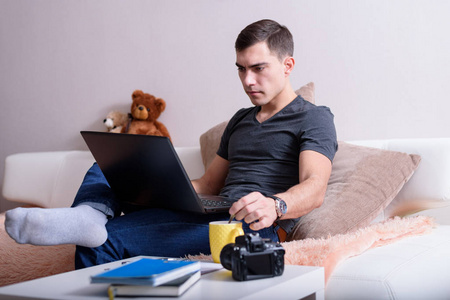 一个现代人坐在沙发上, 上面放着一台笔记本电脑, 还有一个黄色的杯子, 旁边是桌上的笔记本和照相机。自由职业者的概念, 博客, 