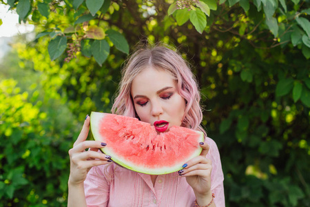 美丽的年轻女子，粉红色的头发，享受着香甜多汁的西瓜