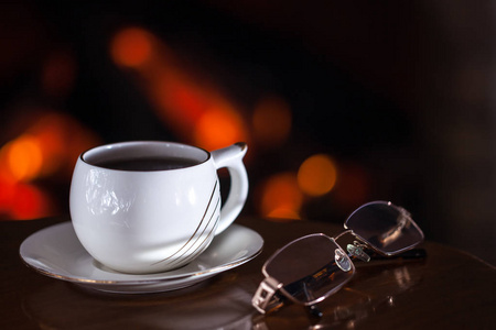 白色杯茶或咖啡和眼镜附近的壁炉木