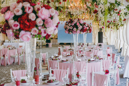 美丽的装饰婚礼宴会下的遮阳篷, 粉红色, 勃艮第和白色色调。用薄布花束花花环和五彩纸屑装饰的餐桌和椅子的大厅