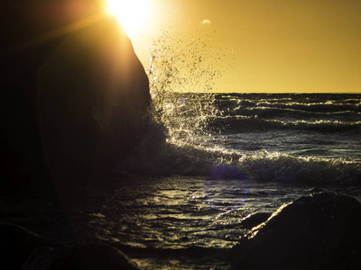 在大石头上溅起的波浪和 backg 的太阳