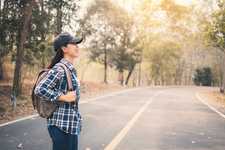 快乐的亚洲女人背包在道路和森林背景下放松时间的假日概念旅行颜色的复古色调和柔和的焦点。