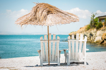 在石滩上用稻草做的躺椅和雨伞。 夏季景观