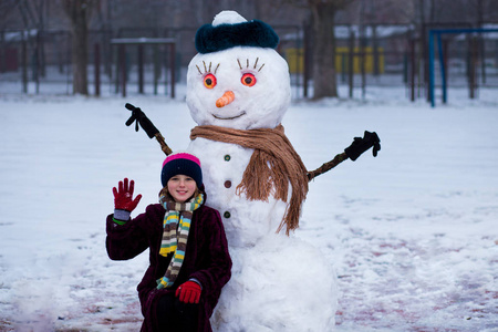 一个快乐的小女孩靠近一个有趣的雪人。 一个可爱的小女孩在冬天的公园里玩得很开心
