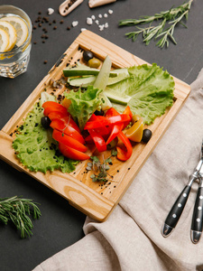 蔬菜沙拉与切片黄瓜，西红柿，胡椒，橄榄和生菜，用柠檬水刀和叉子在木盘上食用