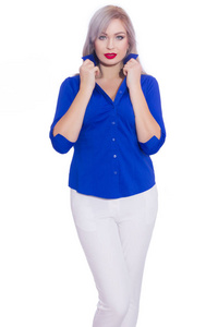 工作室商业肖像一个年轻的金发女人穿着深蓝色衬衫和白色裤子。 女孩在孤立的白色背景上摆姿势。 微笑着看着摄像机
