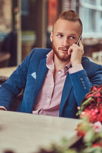 英俊的红发商人，发型时尚，胡子穿着蓝色夹克和粉红色衬衫，在自助餐厅外面打电话。