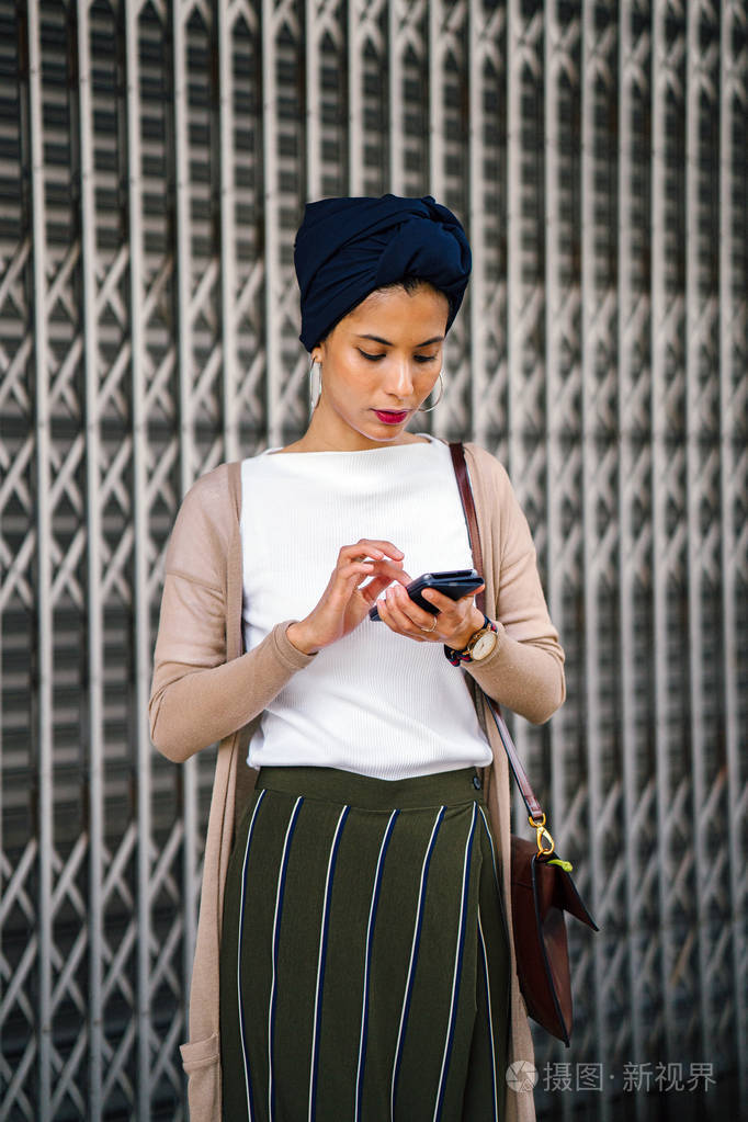 她穿着漂亮的迷彩服,开襟羊毛衫靠在一扇金属