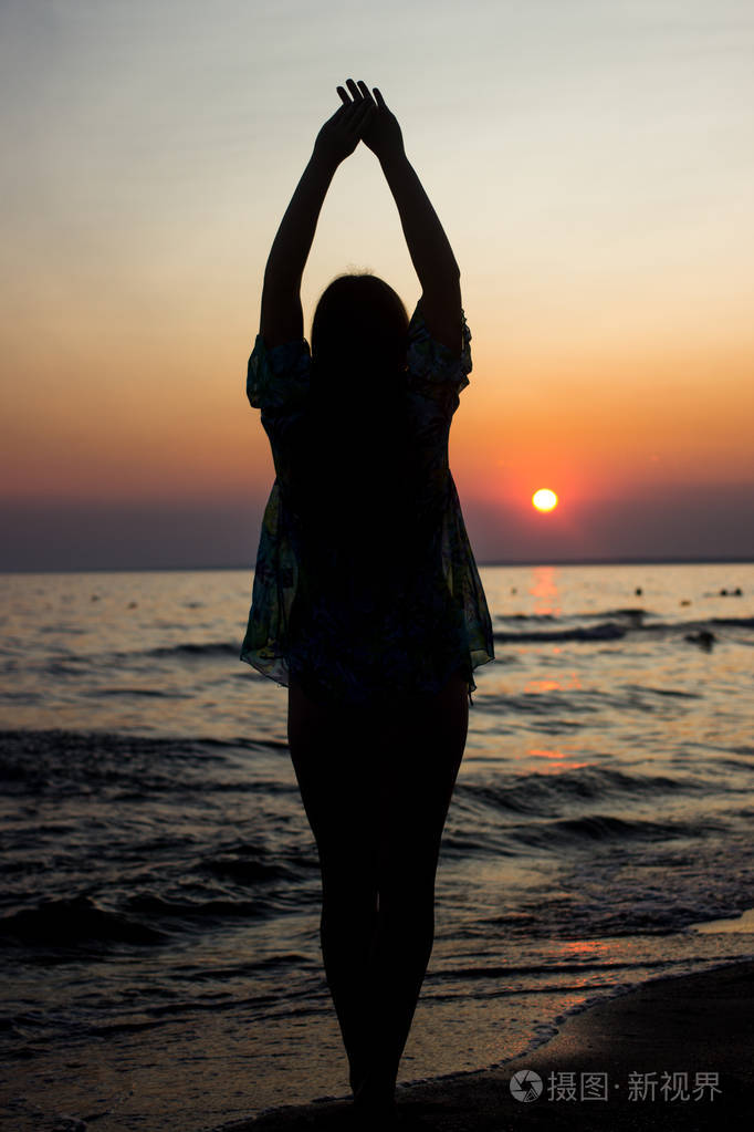 快乐年轻女孩在日落在自然夏天附近的海与他的手举起