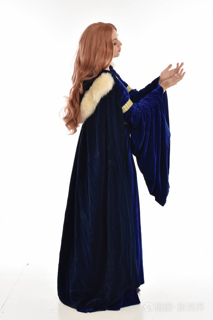 长发女人的全长肖像穿着蓝色天鹅绒中世纪长袍和毛皮斗篷站姿在侧面