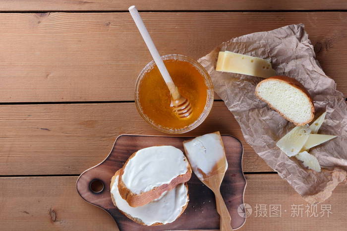 硬奶酪在木板上，食品在羊皮纸上，三明治和软奶酪蜂蜜在玻璃盘子里，复制空间奶酪图案，木制背景餐具，简单的食物