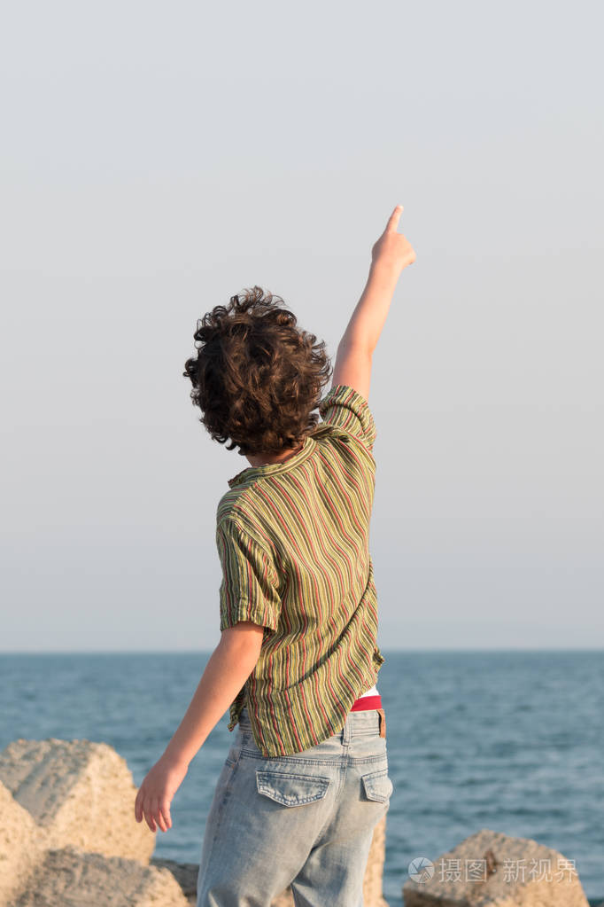 这个男孩站在面对大海的码头上,把手指向天空.