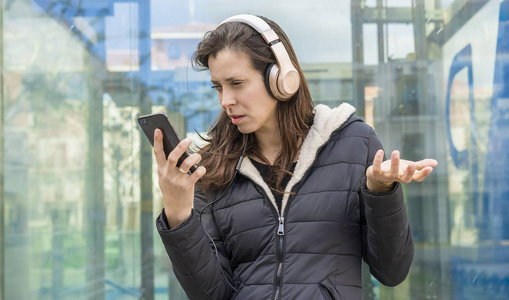 婚姻中的嫉妒和怀疑在手机上的夫妻问题成年女性看着手机上可疑的信息，而在街上用耳机听音乐