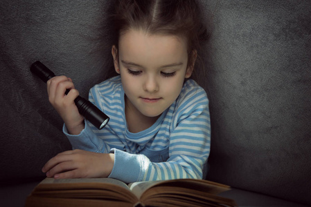小女孩读童话书在夜的盖子之下图片