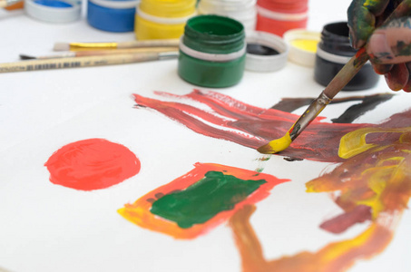 一只孩子的手在颜料上画水彩画在白纸上