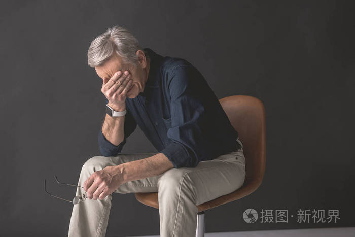 疲倦的高级男性坐在椅子上