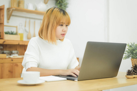 美丽的年轻微笑的亚洲妇女工作在笔记本电脑, 而在家里办公工作空间。女实业家通过笔记本电脑在键盘上写字。在家享受时光