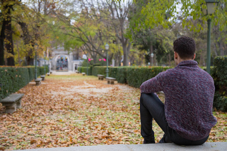 体贴的年轻人坐在秋天公园的楼梯上，看着远处。