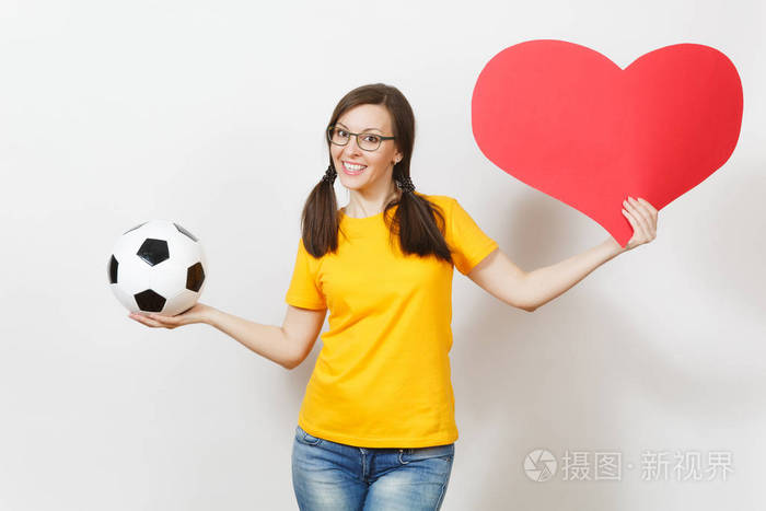微笑的欧洲女人, 有趣的小马尾巴, 足球迷或在眼镜的球员, 黄色制服举行经典足球, 红色的心孤立在白色背景。运动, 足球, 健康
