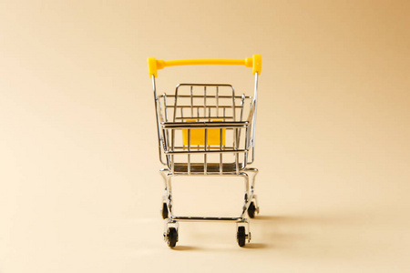 关闭超市杂货推车购物与黑色车轮和黄色塑料元素的手柄上, 在米色背景上隔离。购物的概念。复制广告空间