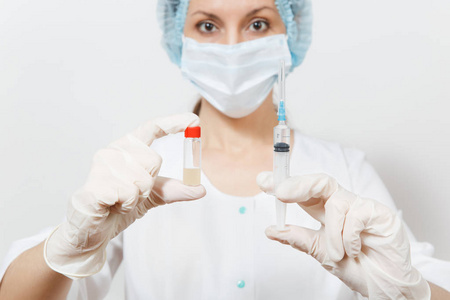 医生在口罩, 无菌帽, 手套持有液体药物瓶与注射器与针隔离在白色背景。女医生的医疗礼服。医护人员理念
