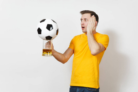 伤心不安的年轻困惑的欧洲人, 球迷或球员在黄色制服举行品脱啤酒杯, 足球欢呼最喜欢的足球队孤立在白色背景。体育, 戏剧, 生活方