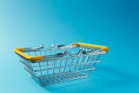 关闭金属杂货篮购物在超级市场与降低手柄和黄色塑料元素隔离在蓝色背景。购物的概念。复制广告空间