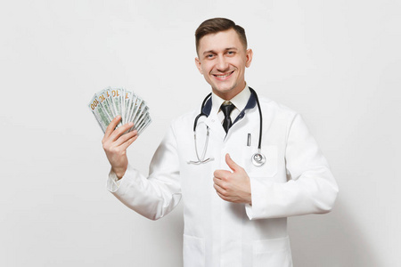 微笑的年轻医生男子孤立的白色背景。男医生在医疗制服上竖起大拇指, 拿着一捆现金钱。医护人员, 健康, 医学概念