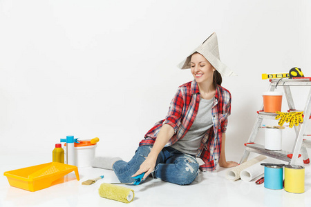 可爱的女人在报纸上戴帽子坐在地板上用油漆辊, 仪器为装修公寓的白色背景隔离。墙纸配件为胶合, 绘画工具。修复主页概念