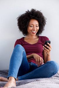 幸福的年轻非洲女人在家里用手机放松的肖像。