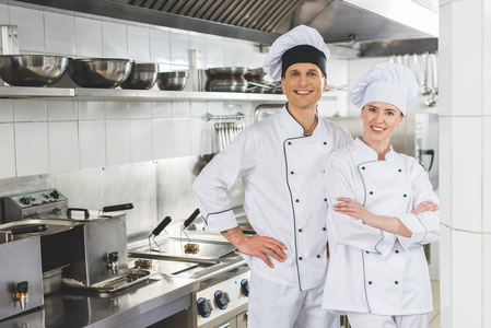 微笑的男厨师和女厨师看着餐厅厨房的摄像机