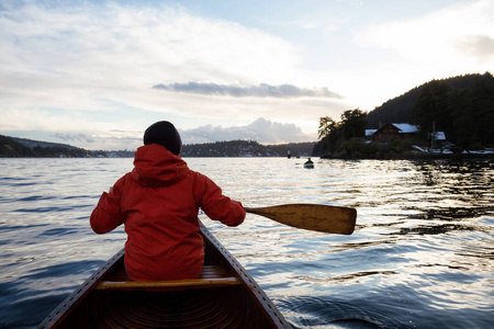 在充满活力的日落中，木舟上的人在划水。 取自加拿大温哥华不列颠哥伦比亚省以北的印度手臂。