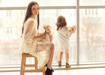 妈妈和女儿站在一个巨大的窗户旁边, 女儿在母亲节那天给妈妈送花。