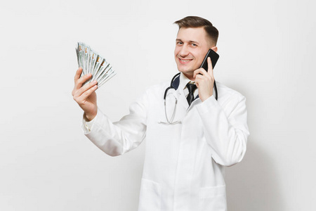 微笑的年轻医生男子孤立的白色背景。男医生在医疗制服上讲手机, 拿着一捆钱, , 现金。医护人员, 医学理念
