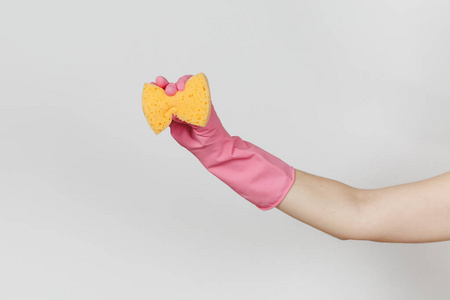 在粉红色的手套关闭女性手举行和挤压黄色橙色海绵清洗和洗涤的菜肴在白色背景下隔离。清洁用品的概念。复制广告空间