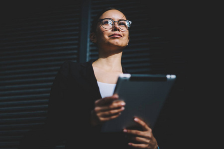 下面是一位女企业家的观点，她戴着光学眼镜和黑色正式西装，手里拿着平板电脑，站在促销背景上看着别人。成功的经理带着触控板